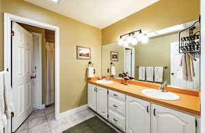 Bathroom featuring double vanity, curtained shower, a skylight, and light tile patterned floors