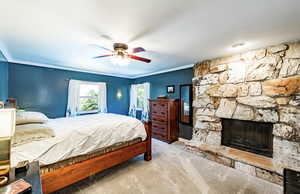 Bedroom featuring ornamental molding, carpet floors, a stone fireplace, and ceiling fan