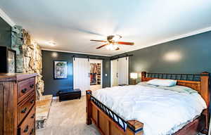 Bedroom featuring ornamental molding, a walk in closet, light carpet, a ceiling fan, and a barn door
