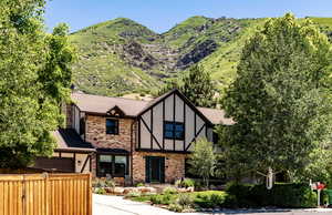 Tudor house featuring brick siding, stucco siding, roof with shingles, a garage, and a mountain view