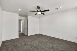 Empty room featuring dark carpet, a textured ceiling, and a ceiling fan