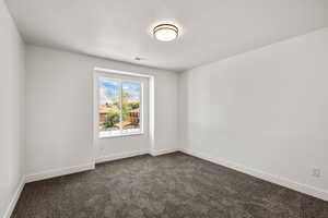 Spare room featuring dark colored carpet and a textured ceiling