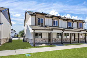 View of front of house featuring roof with shingles, a front yard, board and batten siding, covered porch, and stone siding