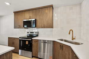 Kitchen with appliances with stainless steel finishes, tasteful backsplash, light stone countertops, and light wood-style flooring