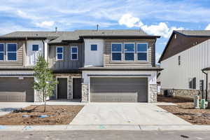View of front of home with stone siding, board and batten siding, concrete driveway, a garage, and a shingled roof