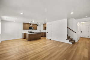 Kitchen with open floor plan, hanging light fixtures, light countertops, a kitchen island, and light wood-type flooring