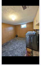 Washroom with wood walls, a textured ceiling, separate washer and dryer, carpet floors, and cabinet space