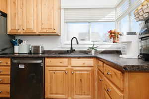 Kitchen featuring dark countertops, dishwasher, light brown cabinets, and stainless steel fridge