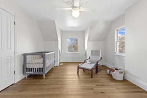 Bedroom featuring a nursery area, light wood-type flooring, ceiling fan, and lofted ceiling