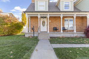 Property entrance featuring a lawn, brick siding, a porch, and roof with shingles