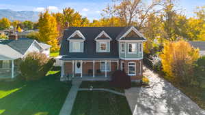 View of front of house with covered porch, brick siding, a front yard, and a chimney