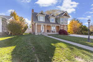 Victorian house featuring a porch, brick siding, a front lawn, a chimney, and roof with shingles