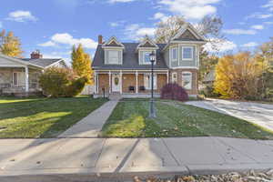 View of front facade featuring a porch, a front lawn, brick siding, and a chimney