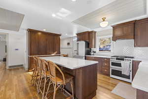 Kitchen featuring white appliances, a kitchen breakfast bar, tasteful backsplash, light wood-type flooring, and light stone counters
