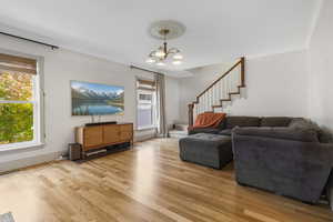 Living area featuring stairway, crown molding, light wood-type flooring, and a chandelier