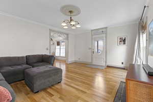 Living area featuring crown molding, light wood-type flooring, and a chandelier