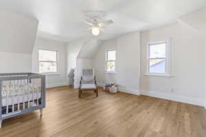 Bedroom featuring light wood-type flooring, a ceiling fan, vaulted ceiling, and a nursery area