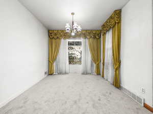 Carpeted spare room featuring a chandelier and baseboards