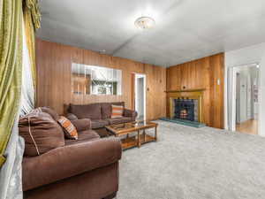 Living area with wood walls, a lit fireplace, and carpet flooring