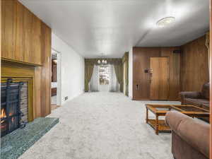 Living room with a chandelier, a lit fireplace, light colored carpet, and wood walls