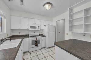 Kitchen with white appliances, dark countertops, and white cabinetry