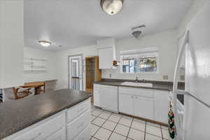 Kitchen with white appliances, white cabinets, dark countertops, and light tile patterned floors