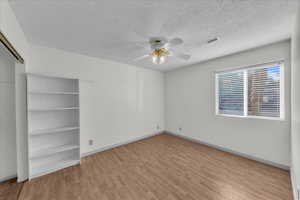 Empty room with light wood finished floors, a textured ceiling, and a ceiling fan