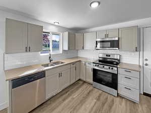 Kitchen featuring appliances with stainless steel finishes, light wood-style floors, backsplash, and light stone counters