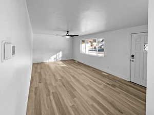 Unfurnished living room featuring light wood-style floors, ceiling fan, and a textured ceiling