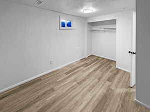 Unfurnished bedroom featuring a textured ceiling, light wood-style floors, and a closet