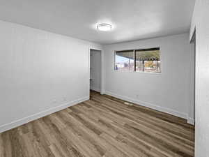Unfurnished room with a textured wall, wood finished floors, and a textured ceiling