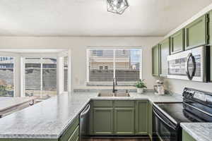 Kitchen with green cabinetry, black electric range oven, stainless steel microwave, light countertops, and a textured ceiling