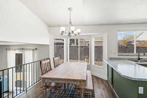 Dining room featuring dark wood-style flooring, a chandelier, a textured ceiling, and vaulted ceiling