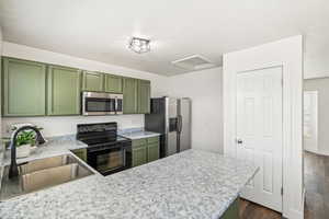 Kitchen with green cabinets, light countertops, stainless steel appliances, dark wood-type flooring, and a peninsula