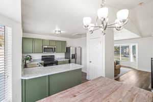 Kitchen featuring green cabinets, stainless steel appliances, dark wood-type flooring, pendant lighting, and a peninsula