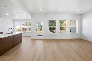 Living room light wood-style floors, recessed lighting, open floor plan, an island with sink, and light stone counters