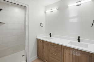 Primary suite bathroom featuring double vanity and tiled shower