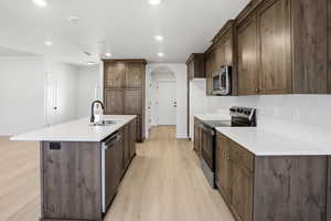 Kitchen with stainless steel appliances, arched walkways, light wood-style floors, recessed lighting, and an island with sink