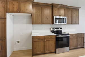 Kitchen with appliances with stainless steel finishes, brown cabinets, light countertops, and light wood-type flooring