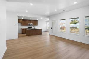 Kitchen featuring open floor plan, recessed lighting, light countertops, a center island with sink, and light wood-style flooring