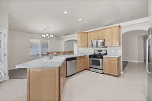 Kitchen with arched walkways, stainless steel appliances, light brown cabinets, light countertops, and vaulted ceiling