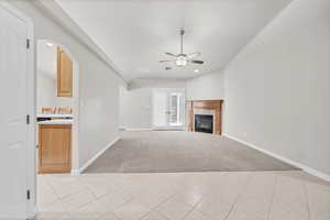 Unfurnished living room with arched walkways, light tile patterned flooring, light carpet, a glass covered fireplace, and recessed lighting