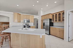 Kitchen featuring arched walkways, glass insert cabinets, light countertops, stainless steel appliances, and light tile patterned floors
