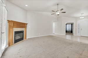 Unfurnished living room with light colored carpet, vaulted ceiling, a fireplace with flush hearth, and a ceiling fan