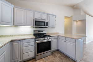 Kitchen featuring appliances with stainless steel finishes, a peninsula, lofted ceiling, and gray cabinets