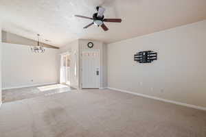 Empty room featuring a chandelier, light carpet, a textured ceiling, a ceiling fan, and vaulted ceiling