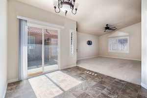 Spare room featuring a chandelier, dark colored carpet, a ceiling fan, vaulted ceiling, and dark stone finish floors