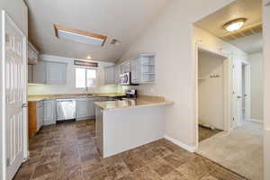 Kitchen featuring open shelves, vaulted ceiling, a peninsula, stainless steel appliances, and dark stone finish floors