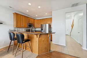 Kitchen with a breakfast bar, a peninsula, brown cabinets, backsplash, and recessed lighting