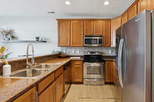 Kitchen featuring stainless steel appliances, brown cabinetry, decorative backsplash, recessed lighting, and light tile patterned floors
